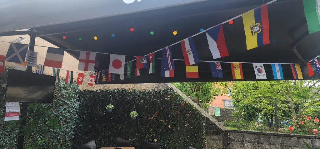 terrasse de café les Bons amis decoré avec les drapeaux des equipes qualifiées pour la coupe du monde 2026 